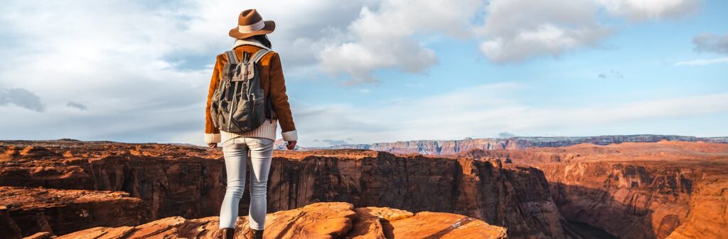 Woman with a backpack and het over looking the Grand Canyon