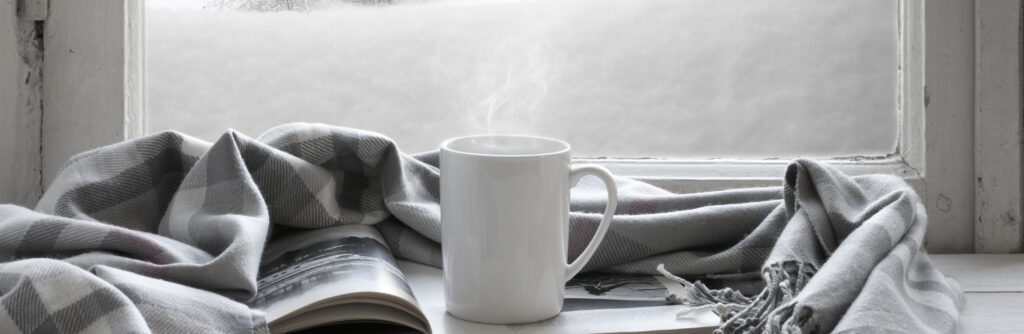 mug with blanket and book in front of a frosted window