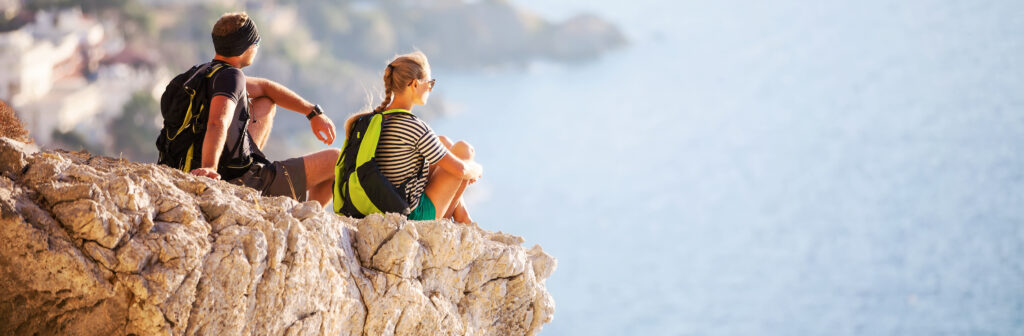 Two people sitting on a rock on a cliff looking at the ocean